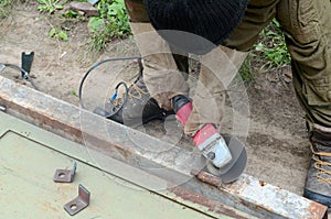 Electric wheel grinding on steel structure outdoors. Old manual worker in protective gloves cutting metal door with grinder