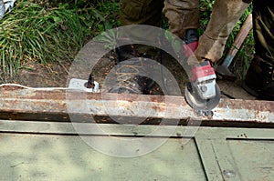 Electric wheel grinding on steel structure outdoors. Old manual worker in protective gloves cutting metal door with grinder