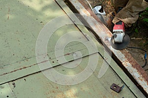 Electric wheel grinding on steel structure outdoors. Old manual worker in protective gloves cutting metal door with grinder