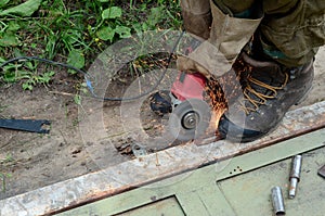 Electric wheel grinding on steel structure outdoors. Old manual worker in protective gloves cutting metal door with grinder