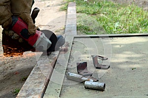 Electric wheel grinding on steel structure outdoors. Old manual worker in protective gloves cutting metal door with grinder