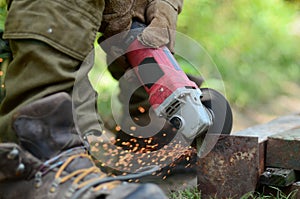 Electric wheel grinding on steel structure outdoors. Old manual worker in protective gloves cutting metal door with grinder