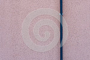 An electric wire on a pink wall. A black live electrical wire is fixed to the wall of a residential building. Electrical