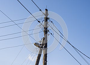 electric wires and a street lamp on an old wooden pole support against a background of blue sky with clouds