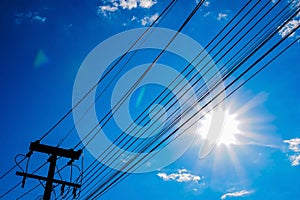 Electric wires stretching along the electric poles against the background of sunlight and blue sky.