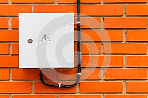 Electrical box with cable and danger sign on a red brick wall.