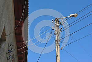 Electrical ceramic fuses and black wires under slate roof on wall and old lantern, view from ground to top, blue sky