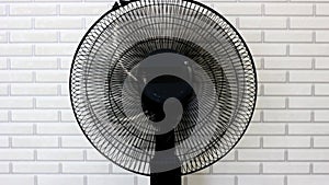 Electrical cooling fan with plastic rotating blades at home in summer on brick wall background.