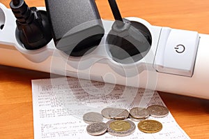 Electrical cords connected to power strip and electricity bill with coins