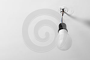 Electrical energy saving light bulb in black chuck hanging on colored wires on a white rough uneven ceiling