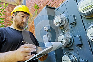 Electrical engineer on during checking in yellow helmet technician examining reading of meter on clipboard