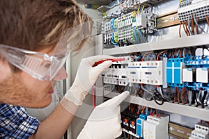 Electrical engineer examining fusebox with multimeter probe