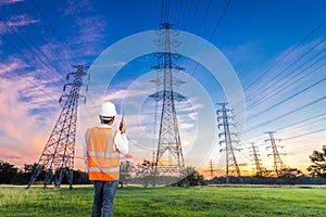 Electrical engineer with high voltage electricity pylon at sunrise background