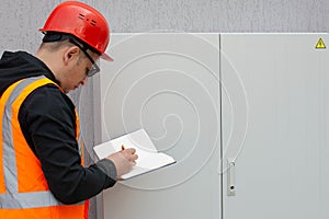 Electrical engineer inspects the switchboard, writing down the faults in a notebook. Maintenance of the transformer photo