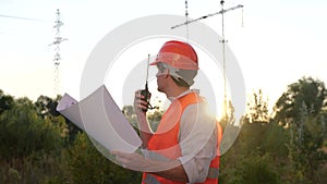 Electrical engineer talking on the walkie-talkie and holding drawing while controlling of repair of electrical high