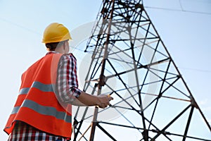 Electrical engineer with walkie talkie near high voltage tower, low angle view