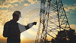 Electrical engineer worker in helmet silhouette working at sunset near the tower with electricity. business energy