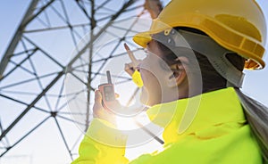 Electrical female engineer using walkie talkie to control a high voltage electricity pylon. Electrical power lines and towers with