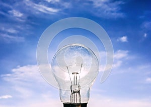 Eelectrical light bulb in hand on blue sky background. Hand holding light bulb on a background sky and sun.