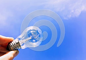 Electrical light bulb in hand on blue sky background. Hand holding light bulb on a background sky and sun.