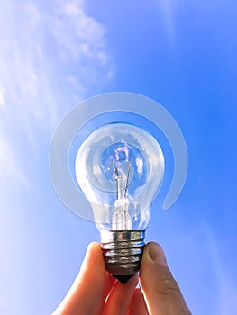 Electrical light bulb in hand on blue sky background. Hand holding light bulb on a background sky and sun.