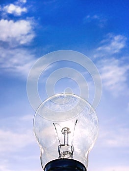 Electrical light bulb in hand on blue sky background. Hand holding light bulb on a background sky and sun.