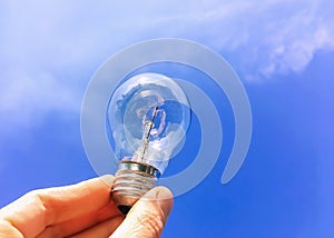 Electrical light bulb in hand on blue sky background. Hand holding light bulb on a background sky and sun.