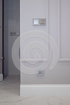 Electrical outlet on brown wall above baseboard and white marble floor. Open invisible hidden door in wall with boiserie in