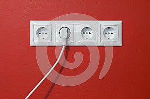 Electrical outlets, cable and electric plug on red photo