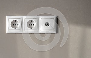 Electrical outlets, a set of empty electrical sockets for appliances and an antenna connector for a TV on an empty gray