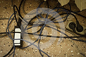 Electrical plugs with cords connected to power strip. Cable power cords in a tangled mess on floor of workplace, used