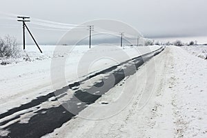 Electrical power lines with hoarfrost on the wooden electric poles on countryside in the winter and winter road