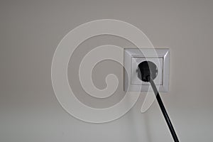 Electrical power socket and single plug black cable switched on, isolated on a plain white wall