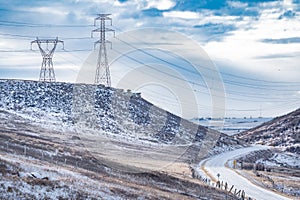 Electrical Pylons on a hilltop with power lines hanging over a valley overlooking winding road in Alberta Canada
