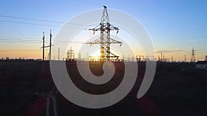Electrical substation against sunset, aerial view of towers of power lines and beautiful sky in backlight