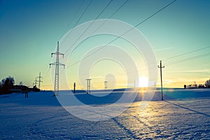 Electrical tower on a snowy field. Sun goes down, orange colors, evening scenery