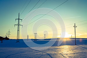 Electrical tower on a snowy field. Sun goes down, orange colors, evening scenery