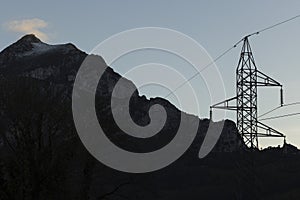 Electrical tower with wires next to high mountain peak with fog