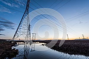 Electrical towers with leading lines at sunset, with reflections in water.