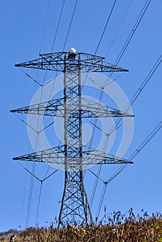 Electrical transmission tower on the top of a hill against a cloudless blue sky