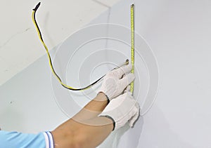 Electrical wiring technician in the house Measure the distance before wiring with the yellow meter tape. Wearing white gloves Two