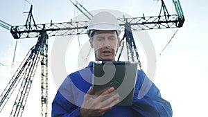 Electrical worker engineer in helmet a working with digital tablet, near tower with electricity. Power business energy