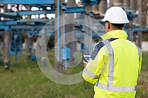 Electrical worker engineer a working with digital tablet, power near tower with electricity. Energy business technology