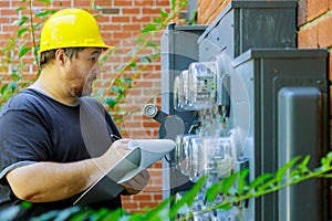 Electrical in yellow helmet technician writing reading of meter on clipboard