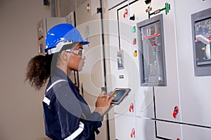 Electrical young asian woman engineer examining maintenance cabinet system electric and using tablet in control room.