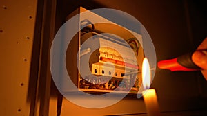 Electrician assembles electrical panel in dark by light of candle. Close up of hand, tightening screw with screwdriver