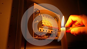 Electrician assembles electrical panel in dark by light of candle. Close up of hand, tightening screw with screwdriver