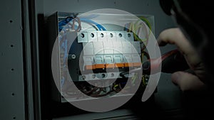 Electrician assembles electrical panel in dark by light of flashlight. Close up of a mans hands tightening a screw with