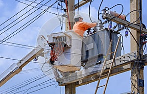 Electrician in bucket of articulated boom lift is repairing electrical transmission on power poles against blue sky