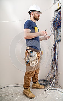 Electrician Builder at work, examines the cable connection in the electrical line in the fuselage of an industrial switchboard.